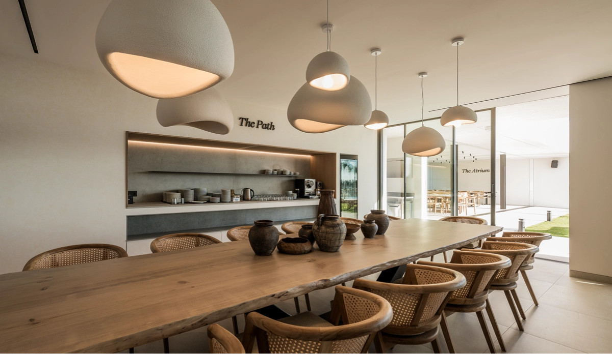 In The Path, you can enjoy a meal in a modern yet cozy dining space. A modern dining area with a long table, comfortable seating, and warm lighting, designed for shared meals and connection among guests at Naghoi.