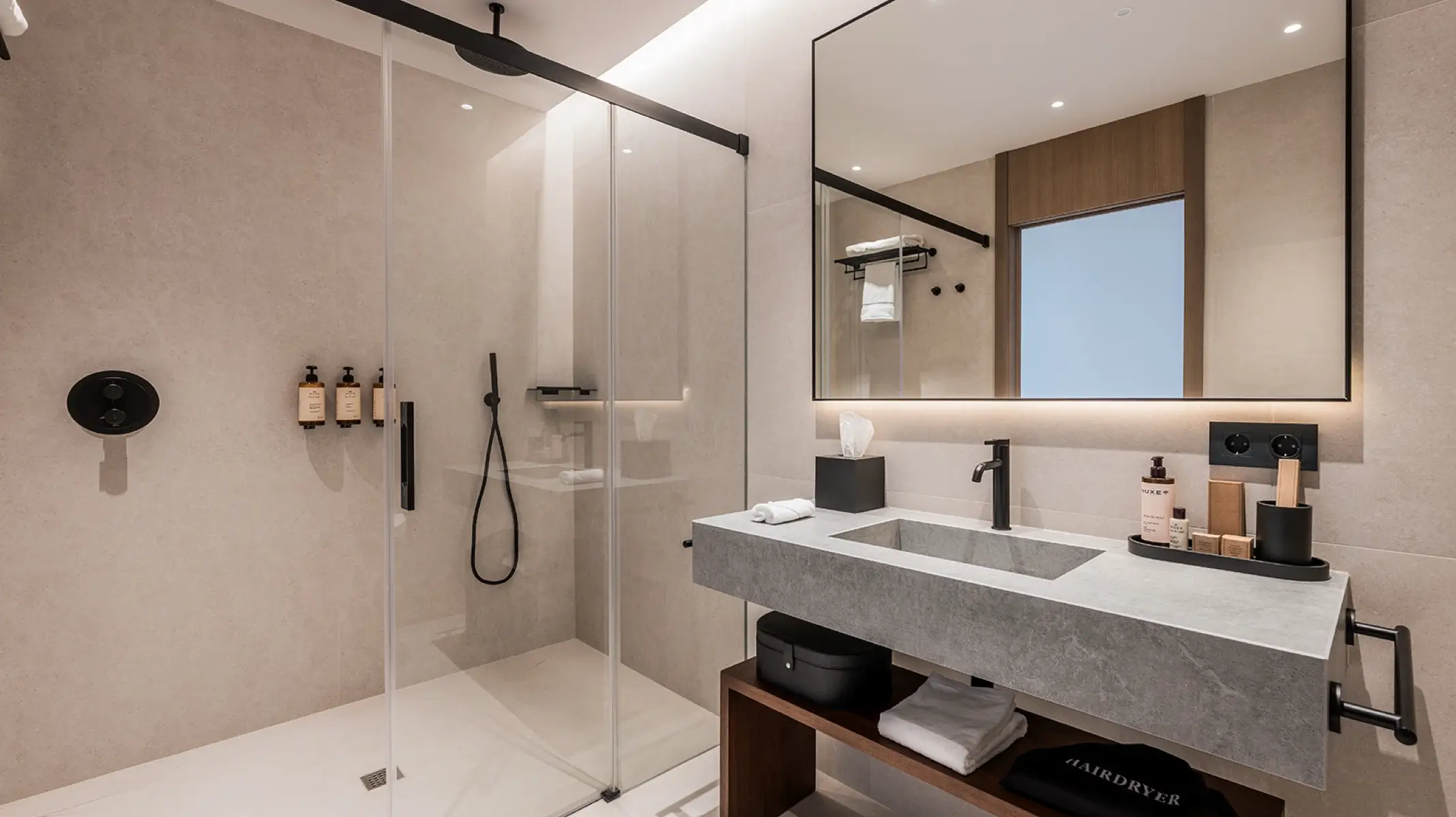 Naghoi guest bathroom — premium stone finishes, glass shower and luxury Nuxe amenities in a post-surgical recovery room in Marbella.